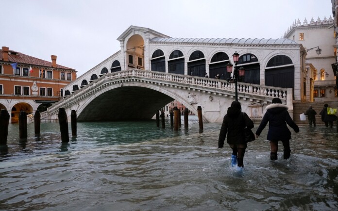 People walk past the Rialto Bridge during high tide as the flood barriers known as Mose are not raised, in Venice